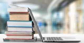 A open laptop leaning on school books.