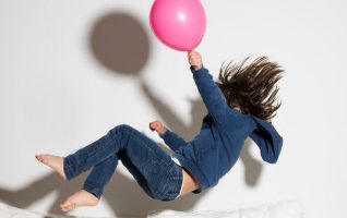 A kid jumping onto a couch holding a balloon.