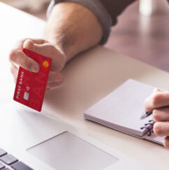 Hand holding First Bank credit card next to laptop
