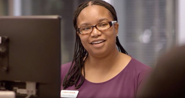 Smiling First Bank employee working at computer.