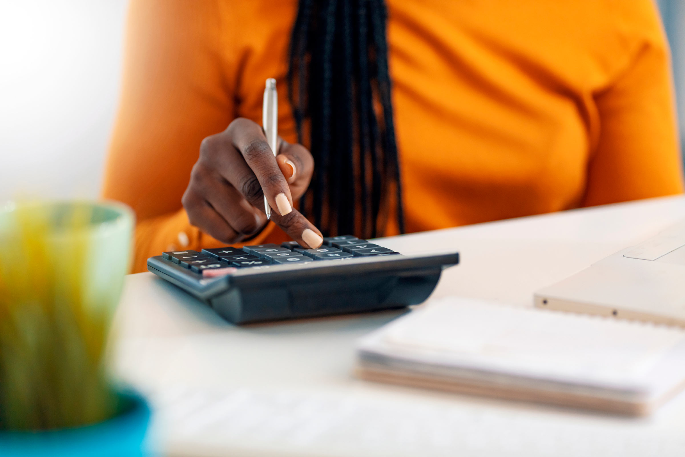 Close up of one African American woman using calculator, calculating finance at home, female hands and paper document at table close up, economist or financier writing report, student doing homework