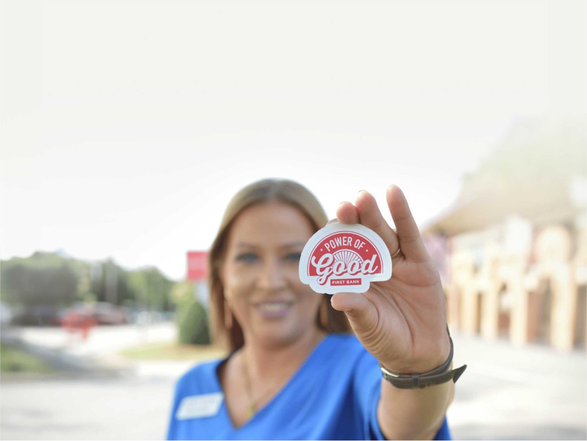 A First Bank employee holding up a Power of Good sticker.