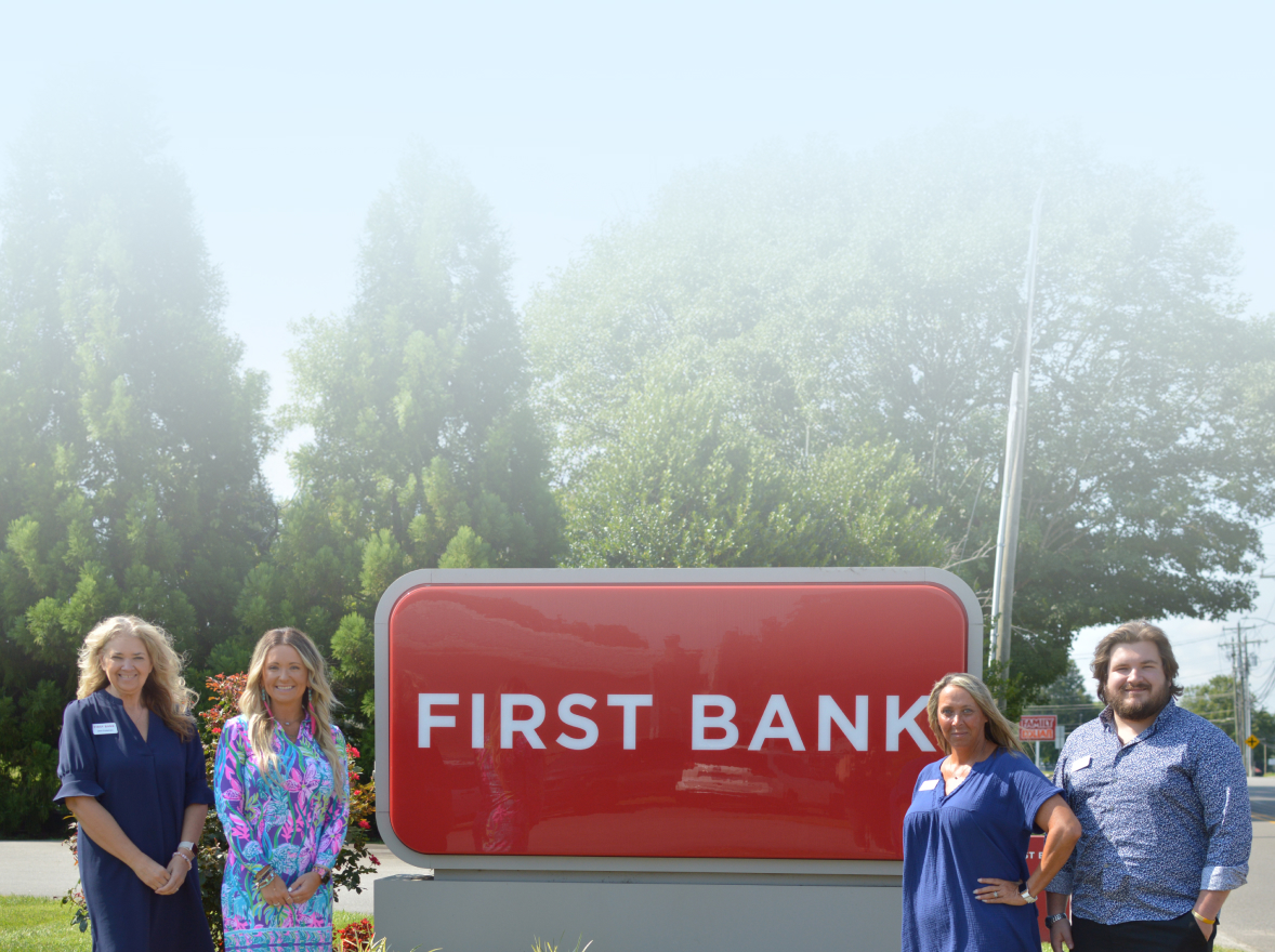 First Bank team members standing next to a First Bank branch sign.